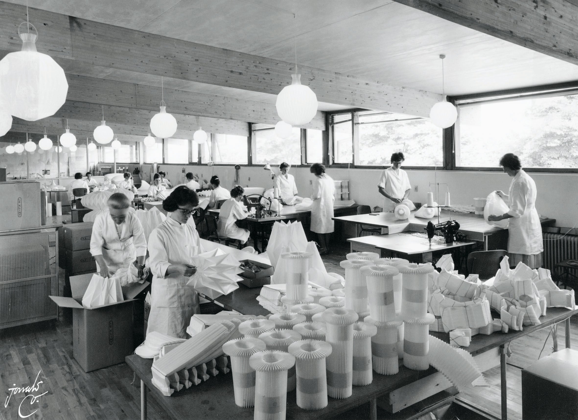 historisk sort/hvid billede af foldestuen hos Le Klint i Odense. Medarbejdere står i hvide kitler og håndfolder lampeskærme.