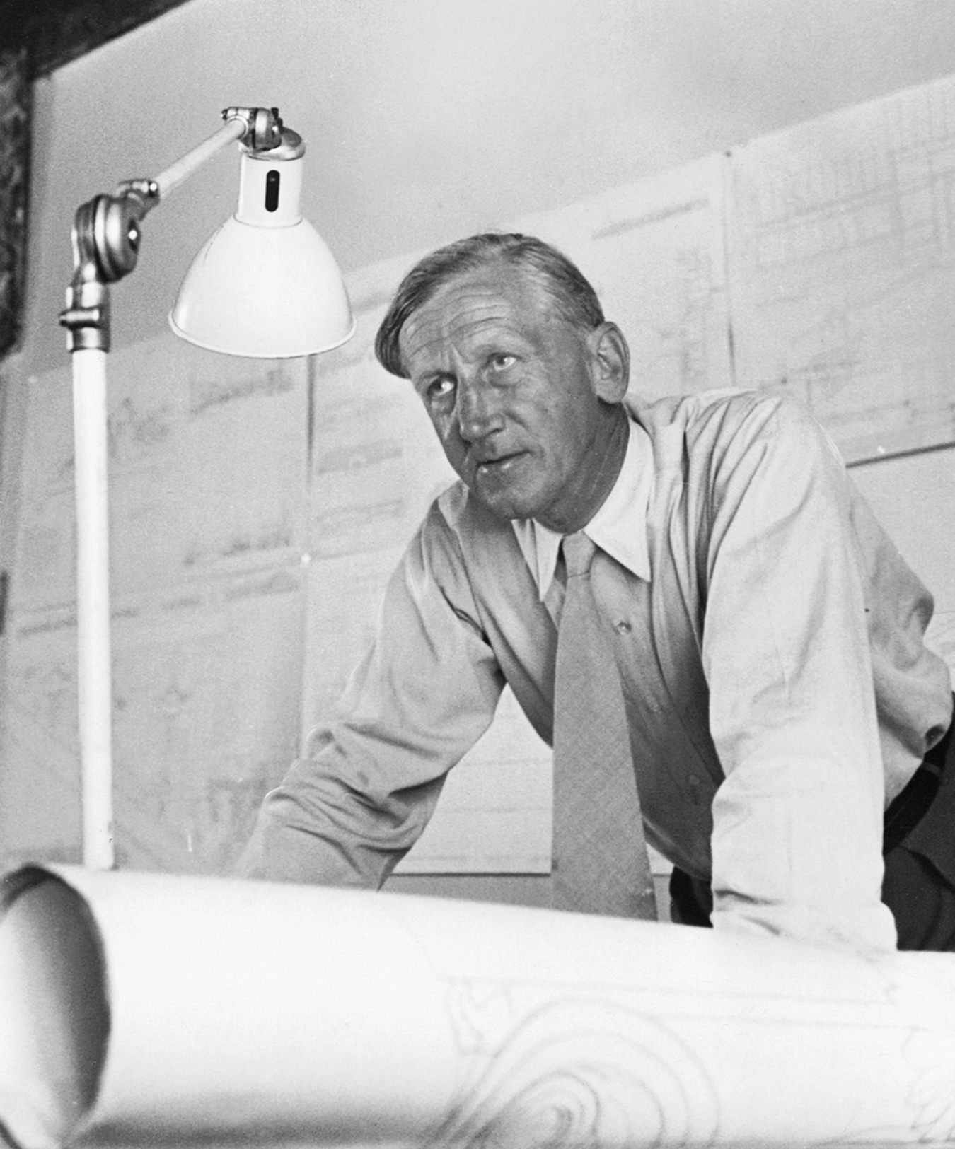 Portræt i sort/hvid af designer og arkitekt Kaare Klint i blandt hans mange tegninger på hans kontor