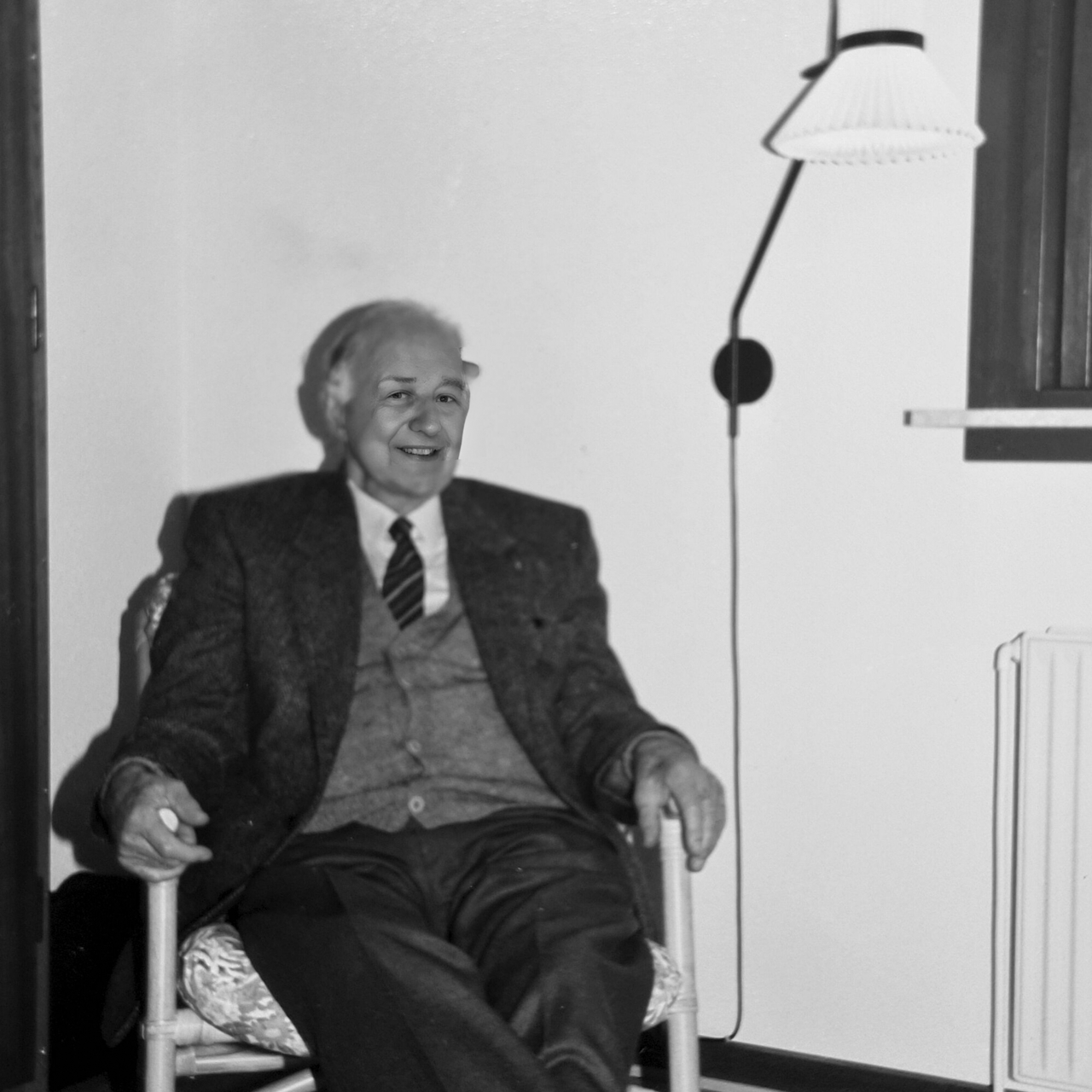 Historisk sort/hvid billede af Jan Klint i en lænestol, ved siden af en Le Klint lampe