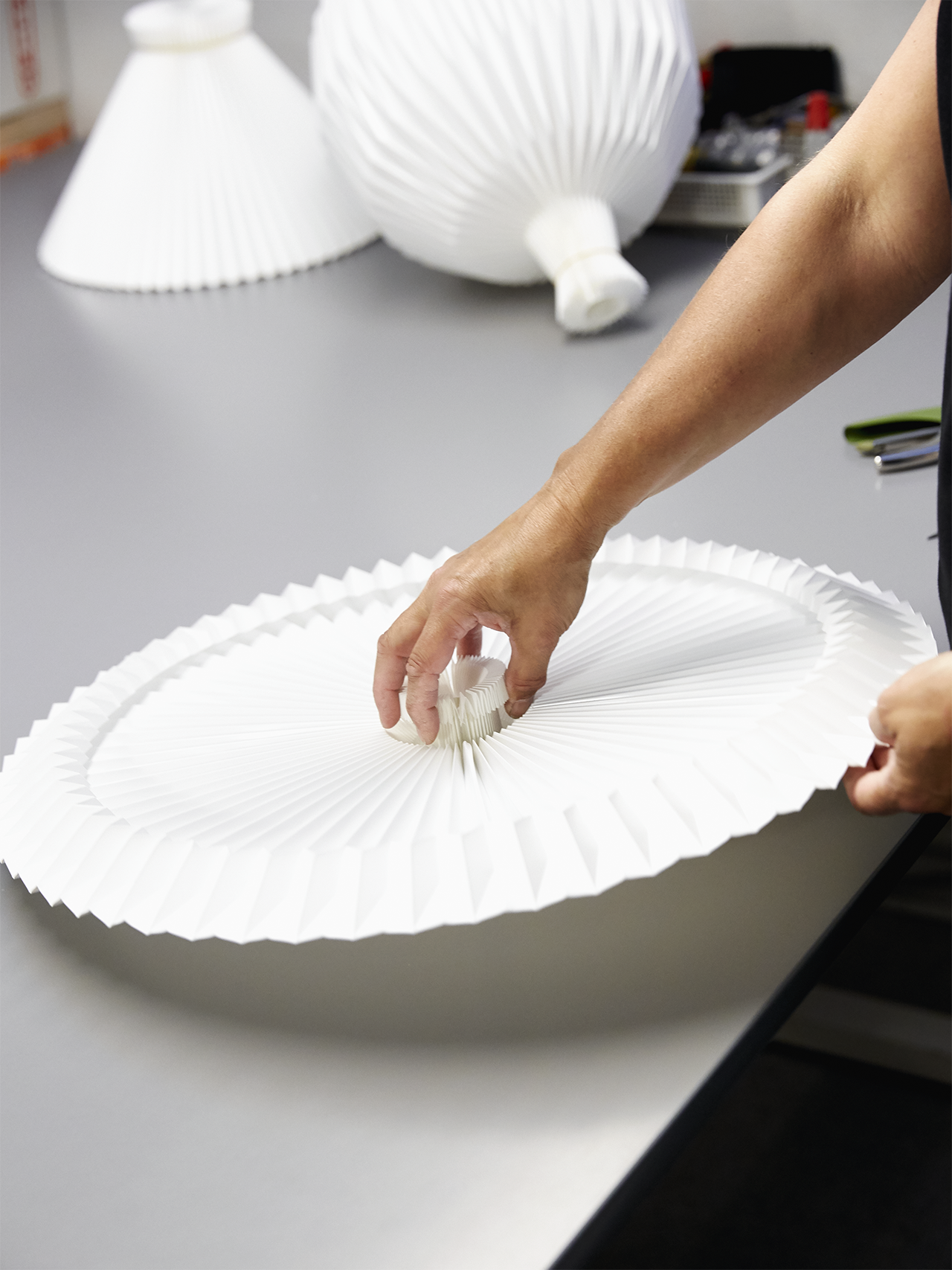 Hænder der vender en håndfoldet plisseret lampeskærm på et bord