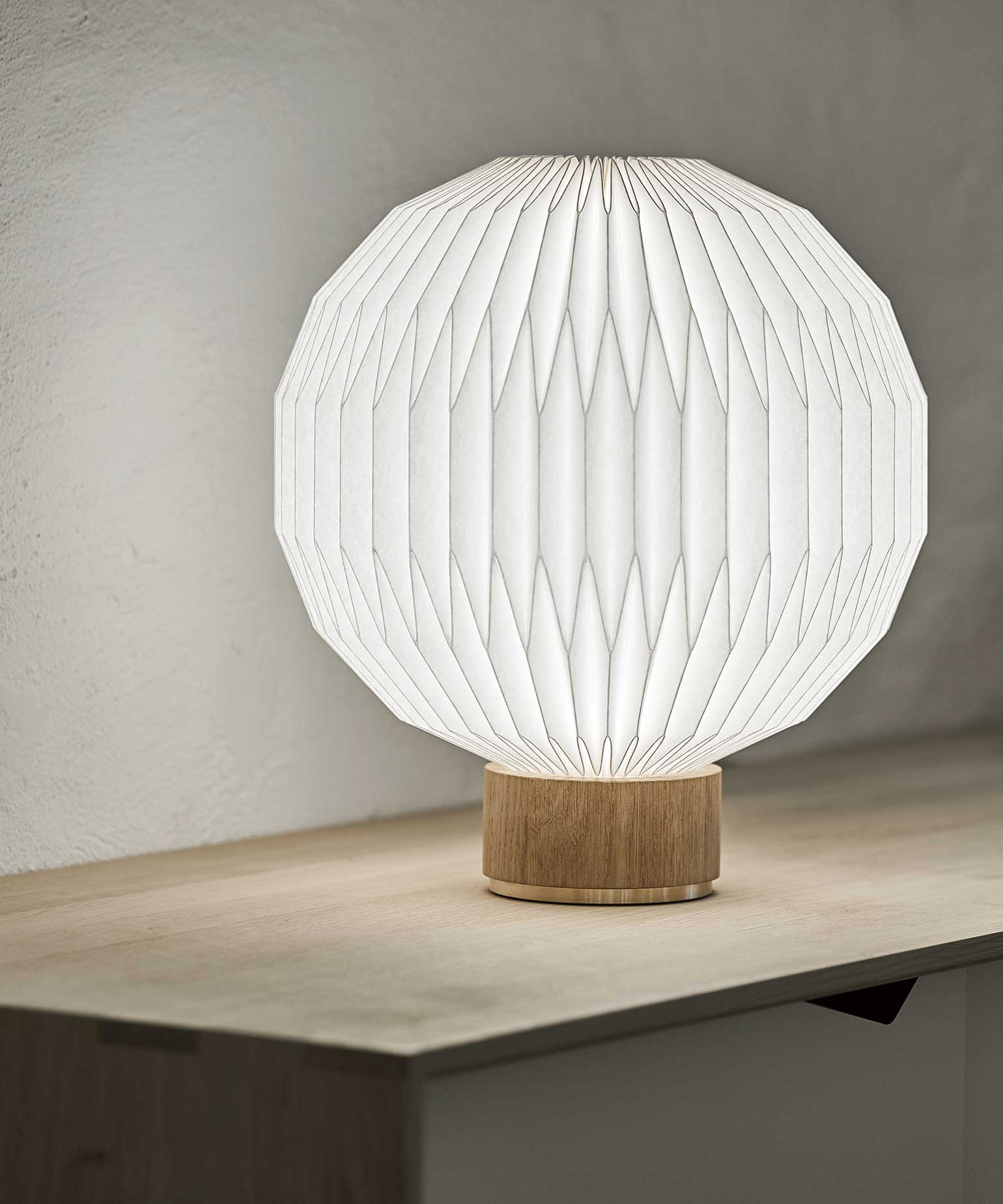 En enkel model 375 bordlampe med fod i lys eg, stående på en reol
