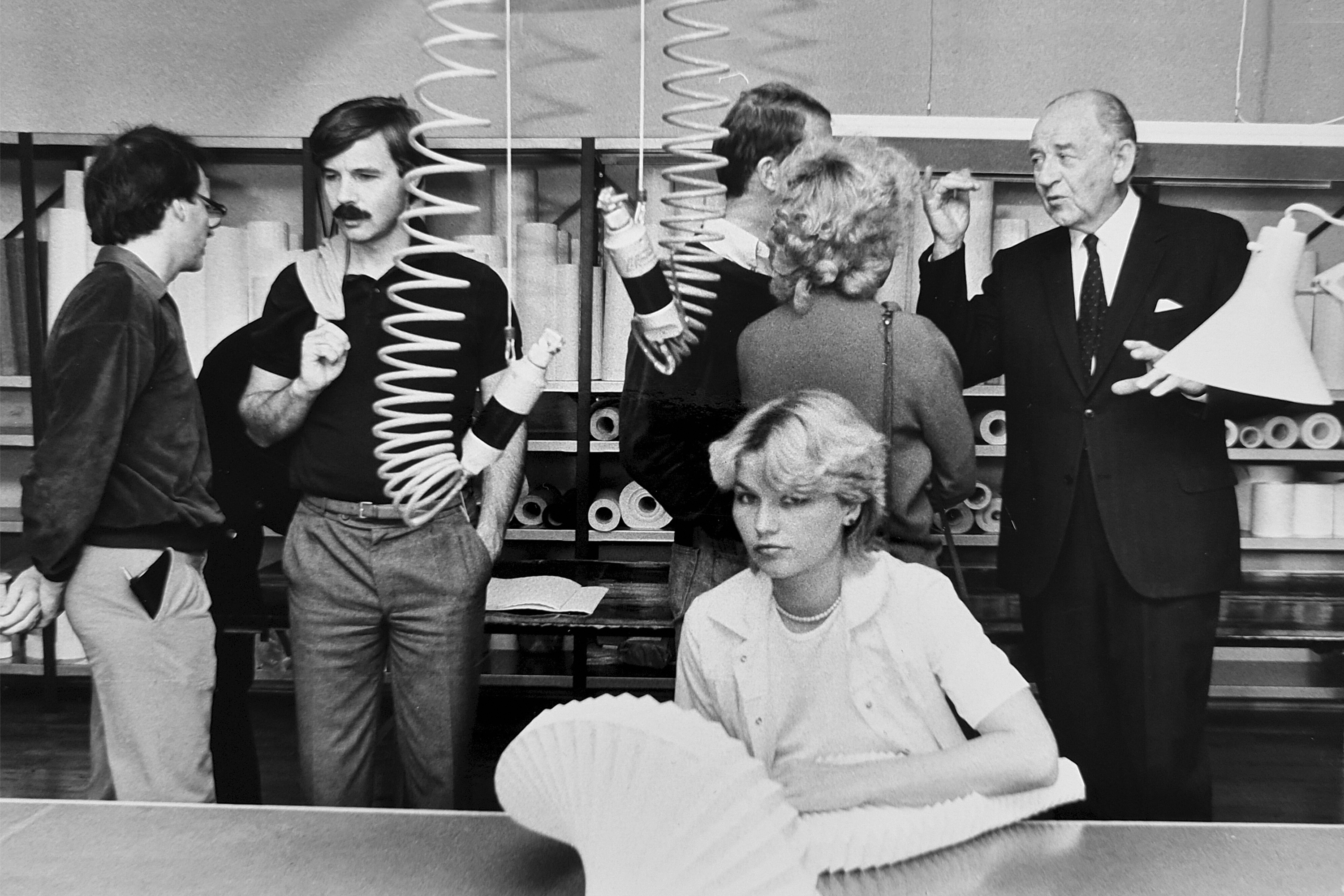 Jan Klint viser rundt på Le Klint fabrikken i Odense hvor en kvindelig medarbejder sidder ved et bord og folder en Le Klint lampe