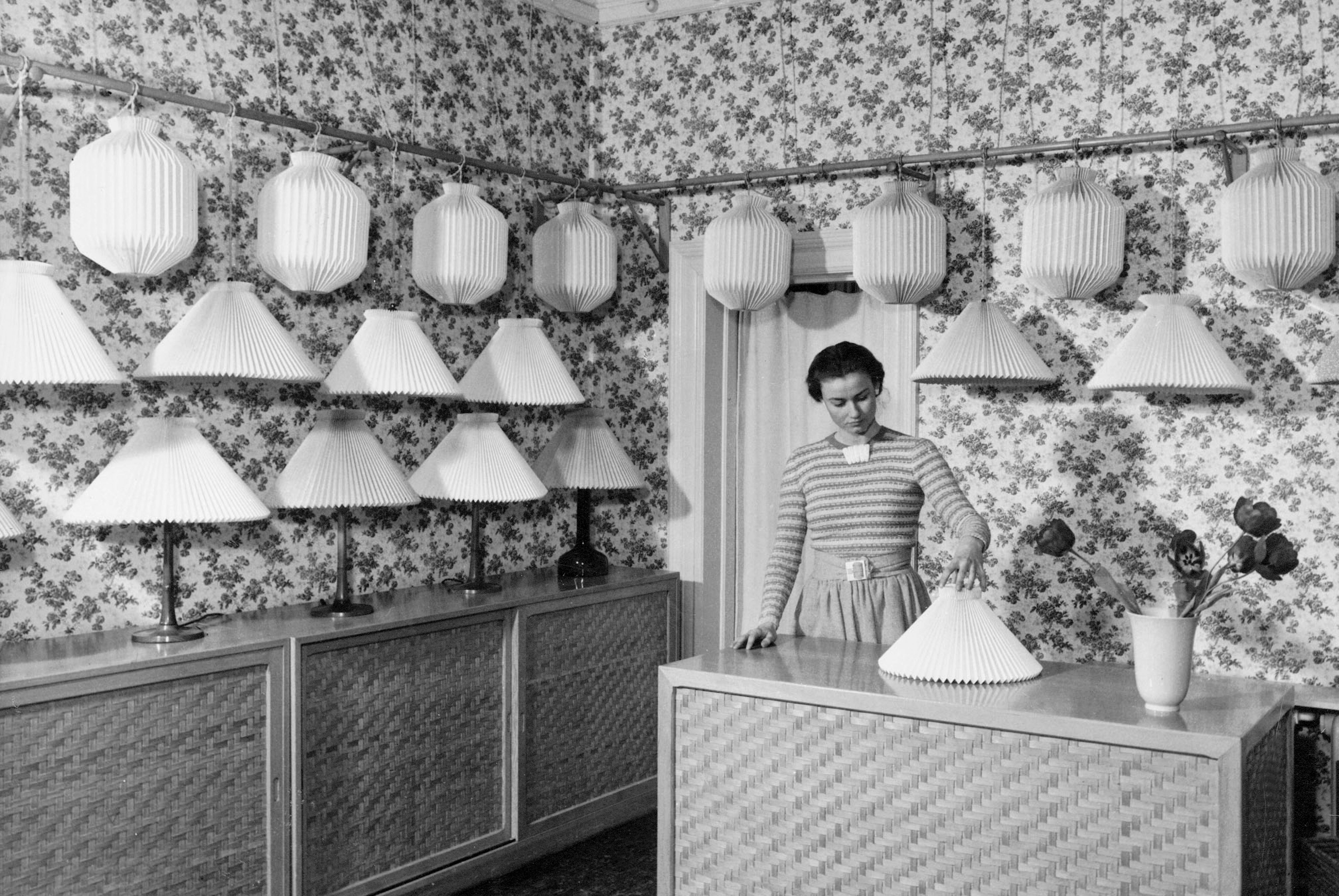 sort/hvid billede af Lise Le stående ved disken omgivet af smukke plisserede lamper i butikken i København